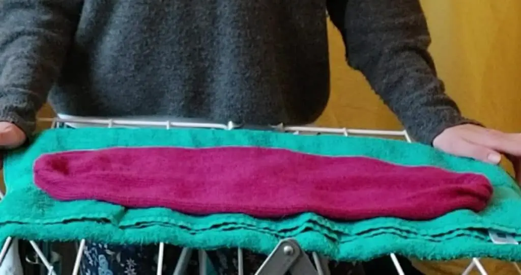 Close up of an alpaca woolen garment drying on a drying rack on top of a towel. 