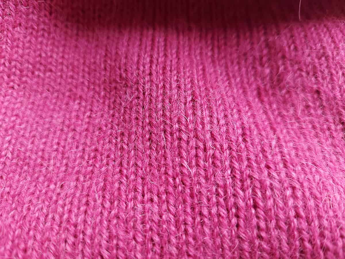 Pink alpaca woolen garment, zoomed in on the fiber, you can see the deails, like springy hairs, shine and smoothness.