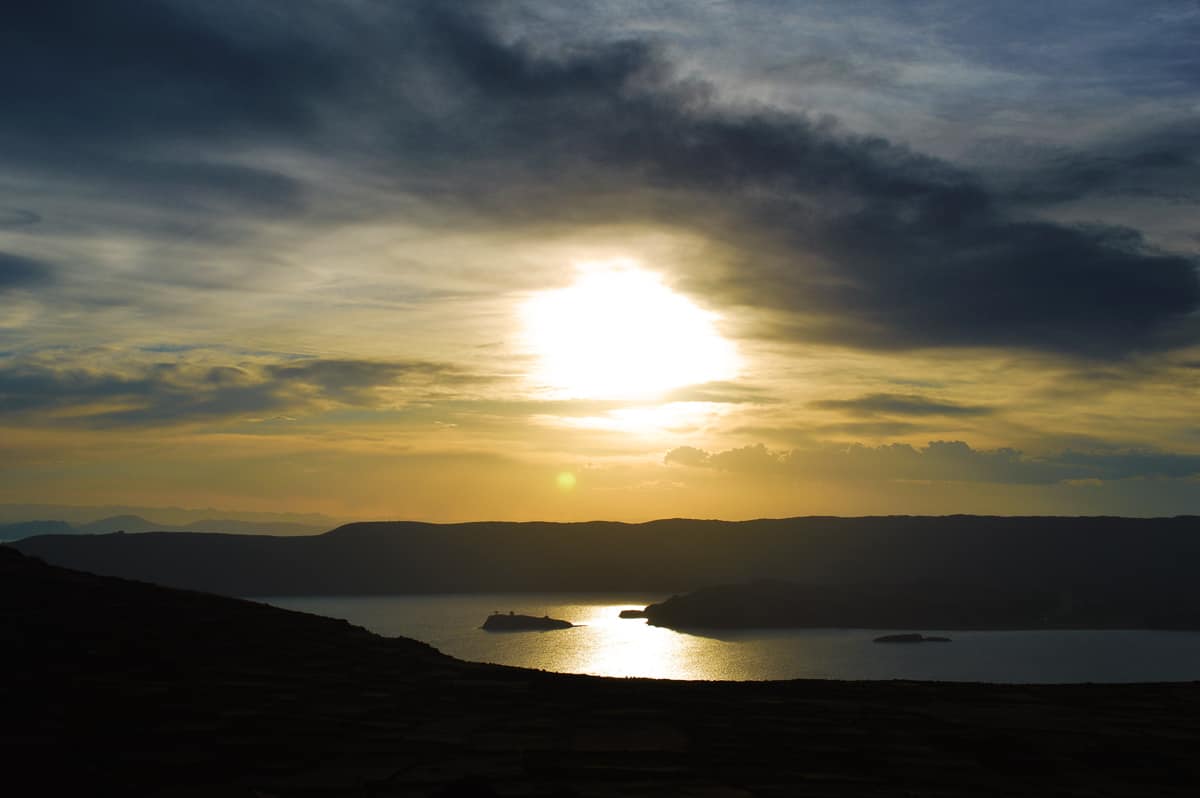 Beautiful sunset on Lake Titikaka in Peru and Bolivia. Half cloudy, half sunny, sun reflects on the water in the lake with mountains in the background.