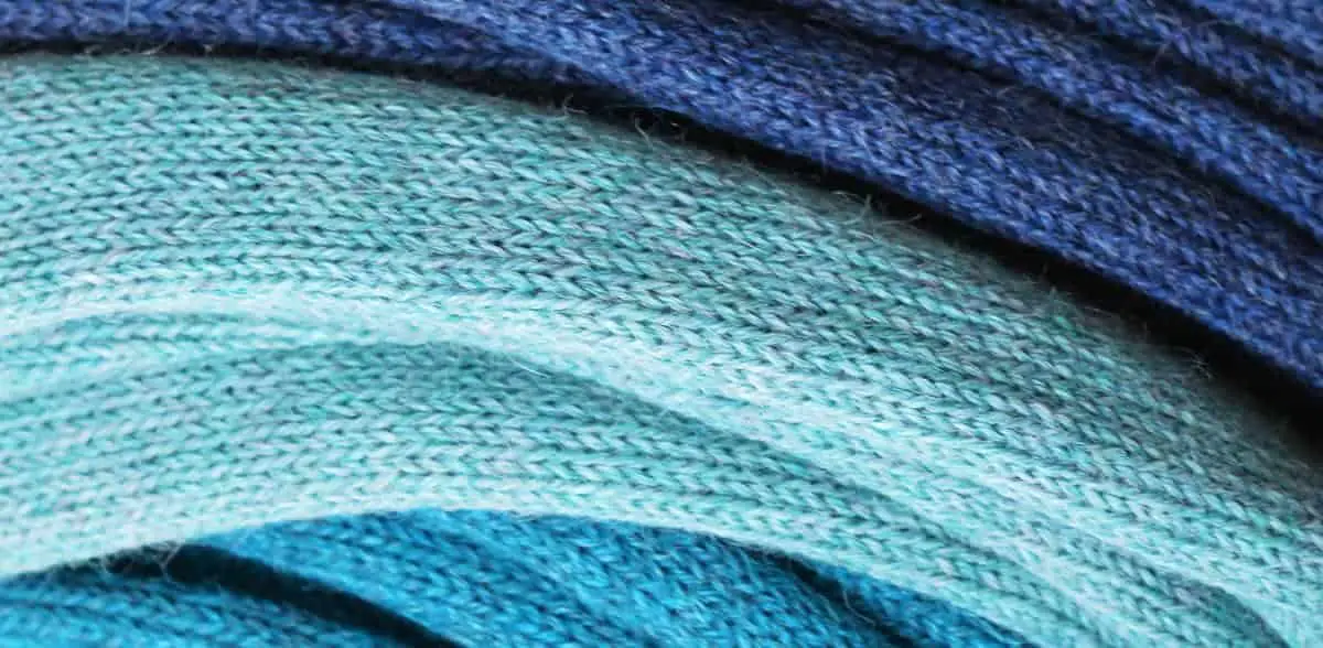 Three alpcaca woolen scarves in different shades of blue, folded and piled up.