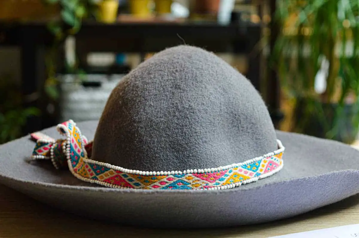 Felted grey hat with a small chord wrapped cord around it. Cord has colors and traditional weaving pattern and small beads on the side.