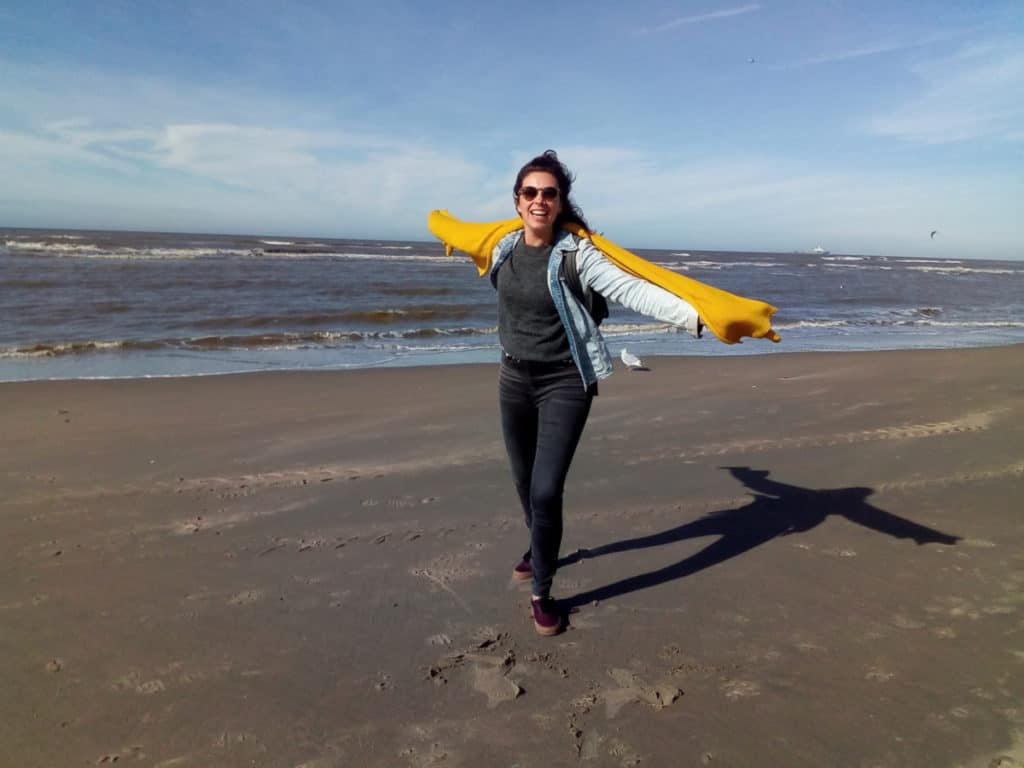 Young woman (Eveline) wearing alpaca woolen scarf on the beach. The weather is windy and sunny and the alpaca woolen scarf protects from both.