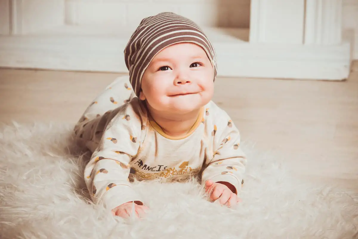 Cute little baby with hat crawling on a furry rug. The baby smiles and looks up to the camera.