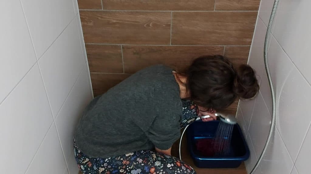 Picture of a woman rinsing an alpaca woolen item in a tub with cold or lukewarm running water. 