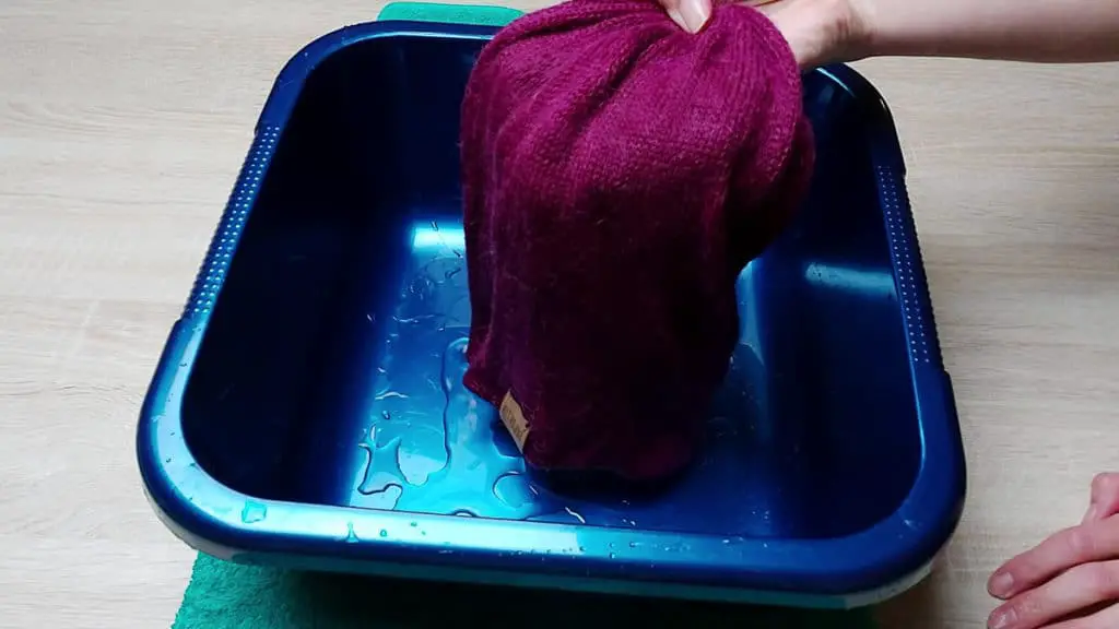 Image of a wet alpaca woolen hat. You can see how much water has been absorbed. The garment looks heavy and soaked and the water is dripping out of the garment. 