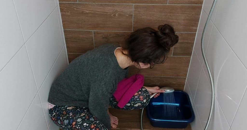 Image of a woman filling a tub with cold / lukewarm water before adding in the alpaca wool product. 
