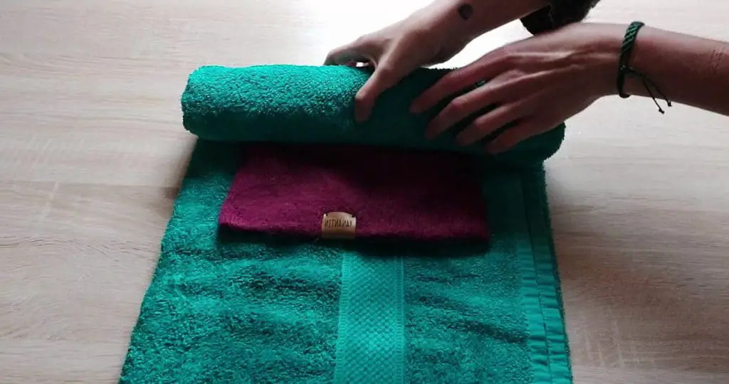 Image of an alpaca woolen hat between a towel that is being rolled up to remove water from the garment. 